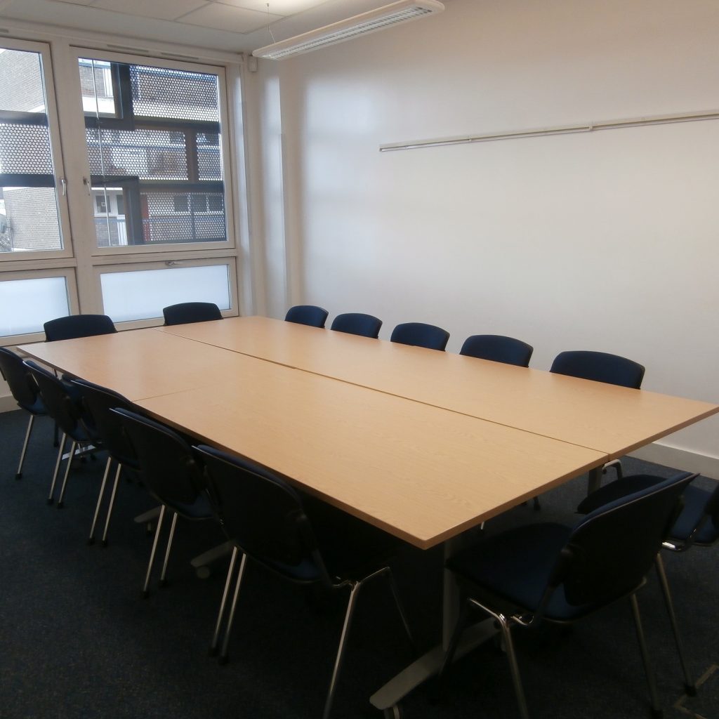 Meeting room with white walls, window at far end and tables and chairs in boardroom layout with 12 chairs