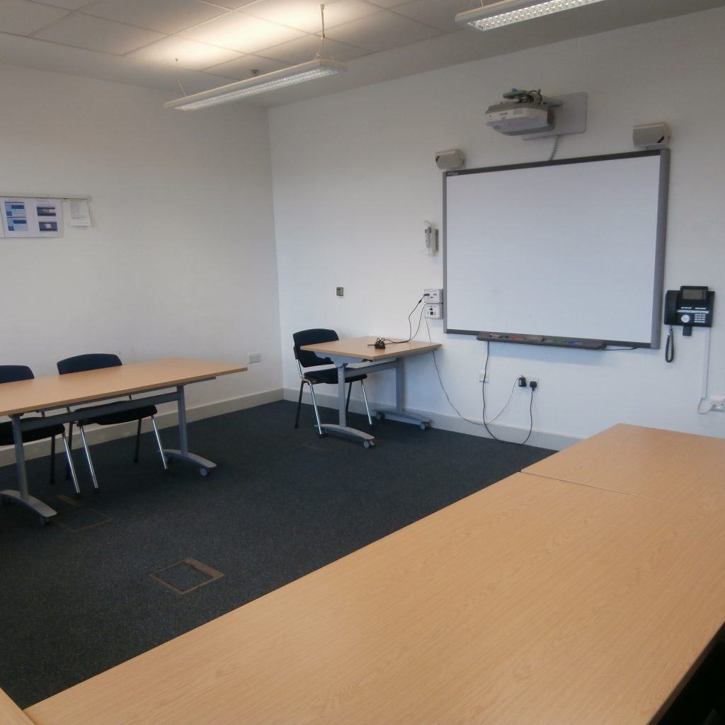 Medium size meeting room with whiteboard at far end and tables in U-shape with chairs