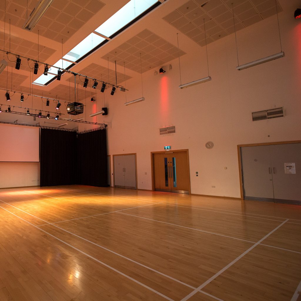 Large Hall with lighting rig, light wood floor and projection screen on the back wall.