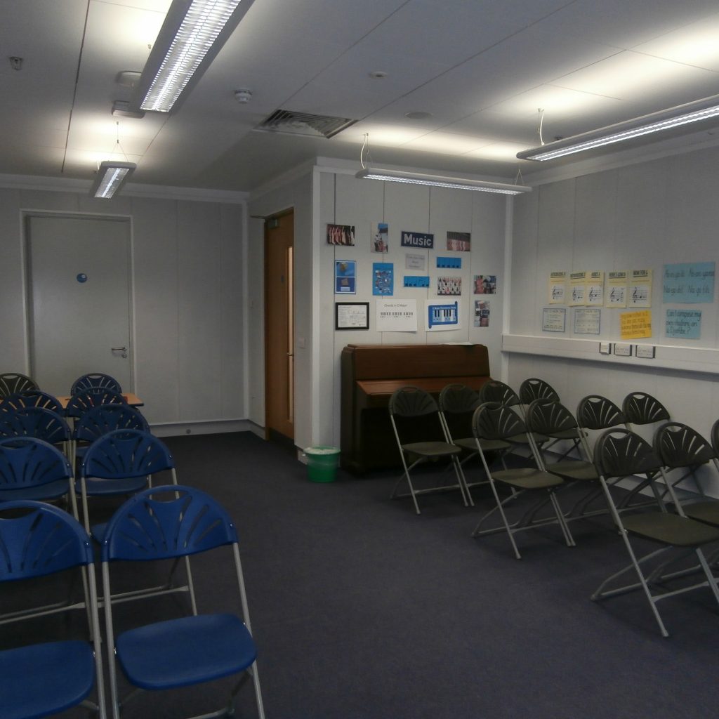 Spacious room with chairs in rows an a piano in the back, right corner..