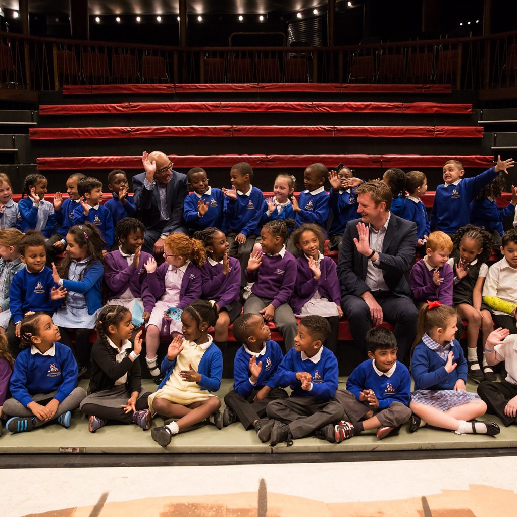 Picture of a large group of 4 and 5 year old kids waving in a theatre.