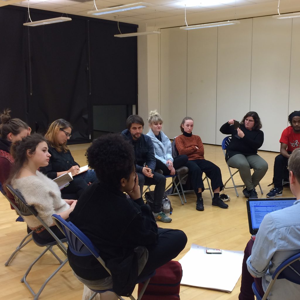 Young people seated in a circle in a light coloured rehearsal room.