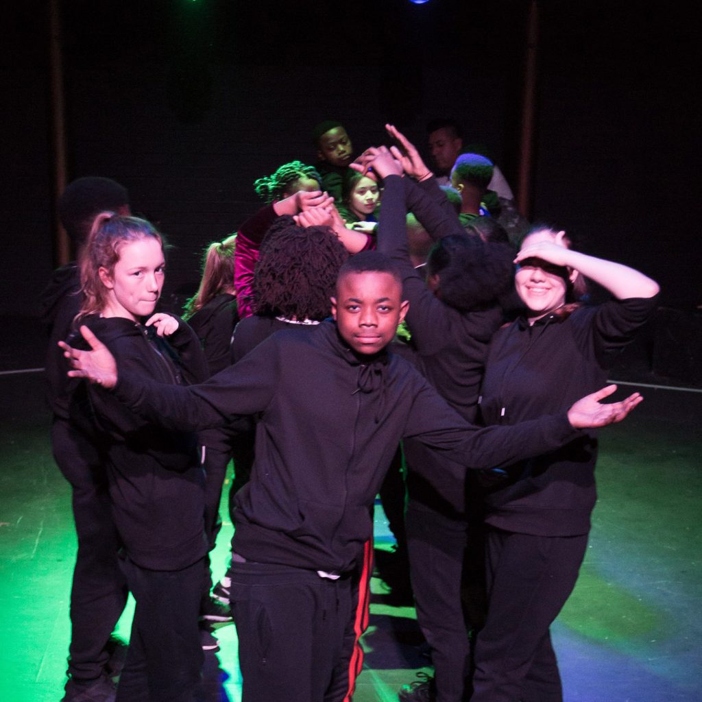 Young dancers in tableaux on stage wearing black tracksuits.