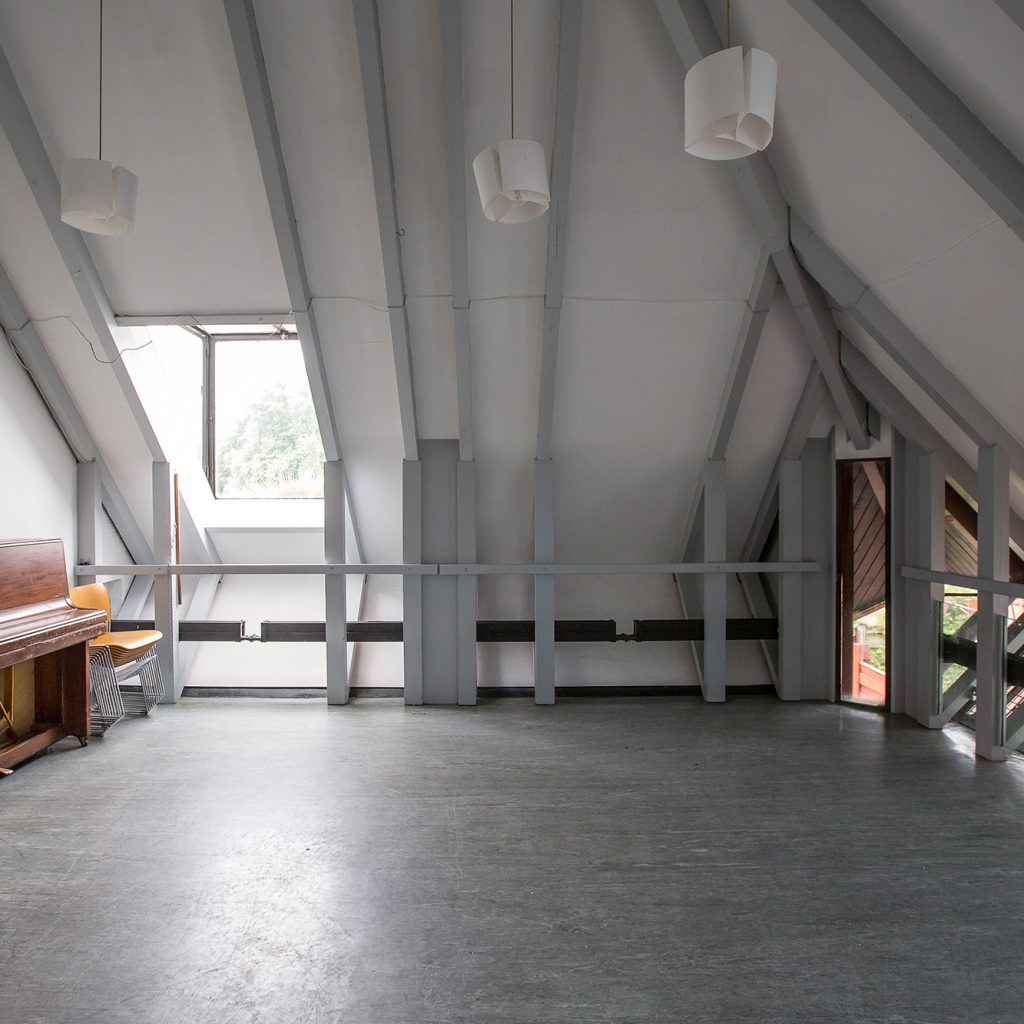 Square, empty room with natural light and a piano.