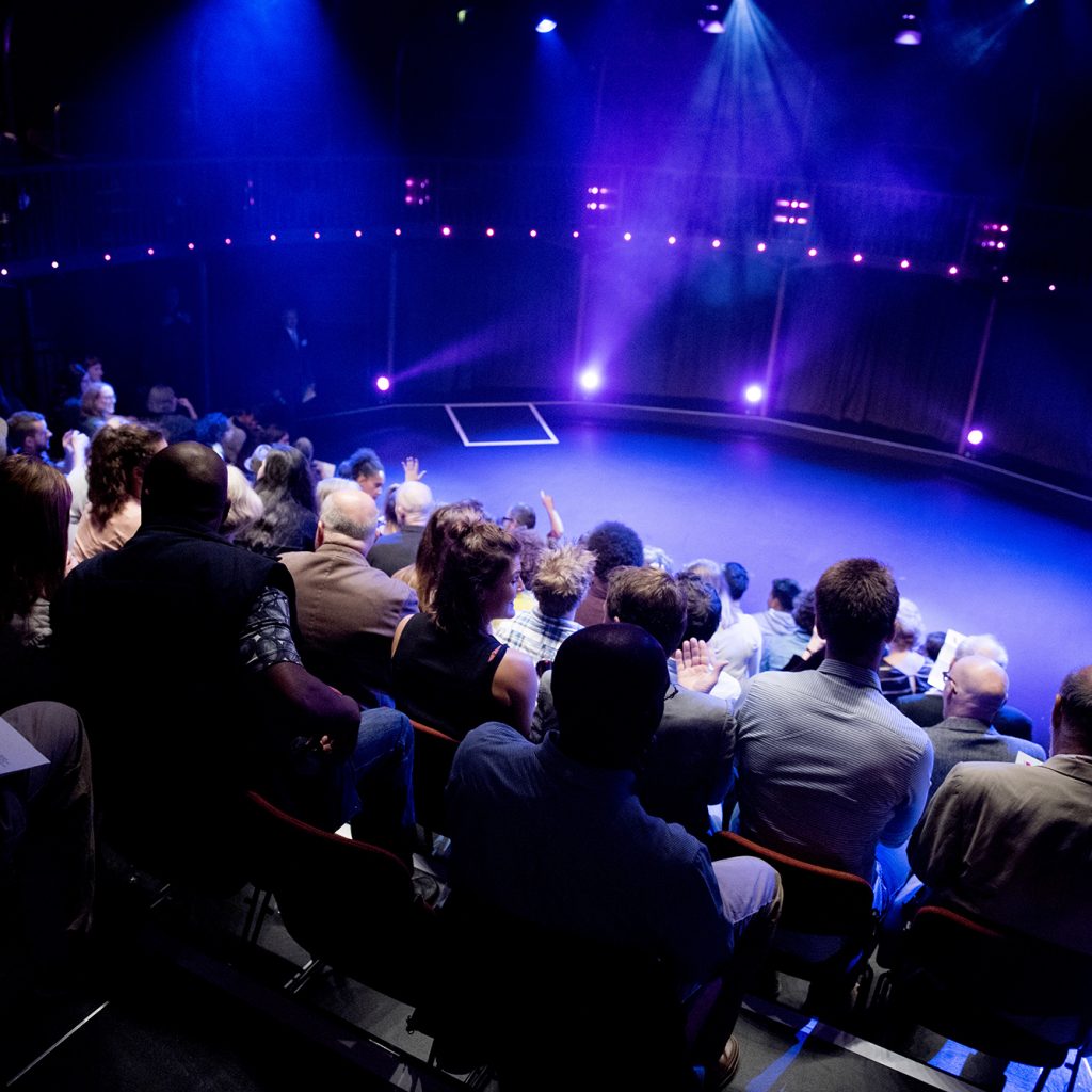 Image from the back of the Albany theatre of an empty stage and full seats, people waiting for a performance to begin.