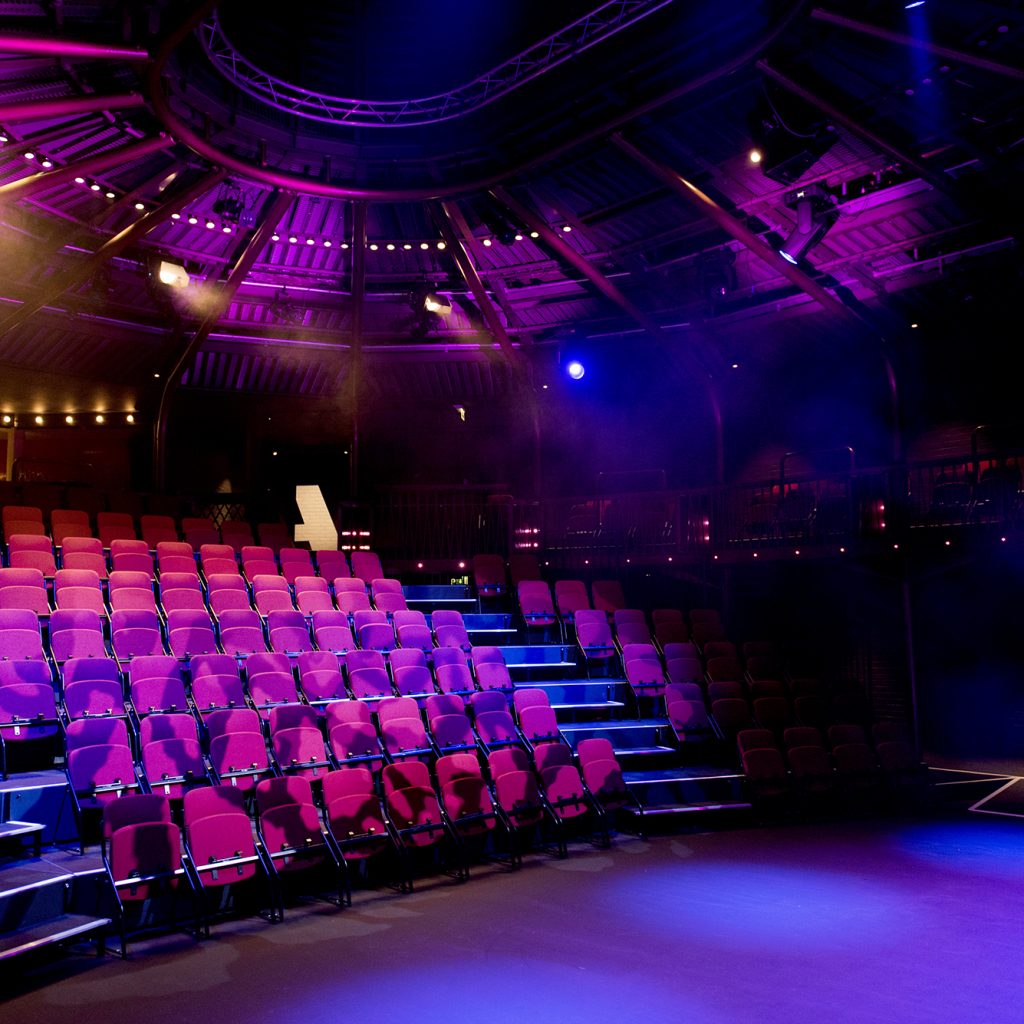 Large theatre auditorium pictured from the stage with brown seats.