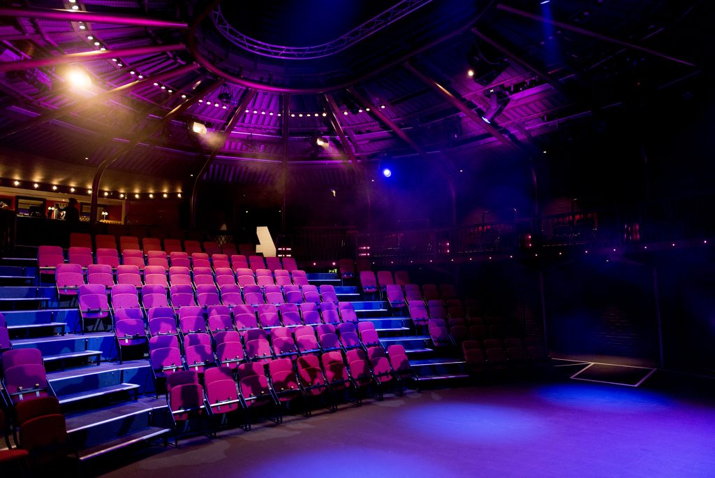 Large theatre auditorium pictured from the stage with brown seats.