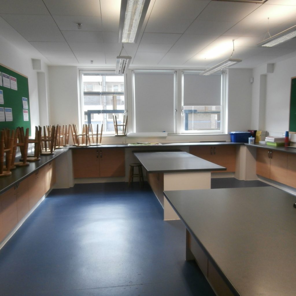 Large professional style food-preparation area with island and wall ajoining worktops. Windows at back of room.