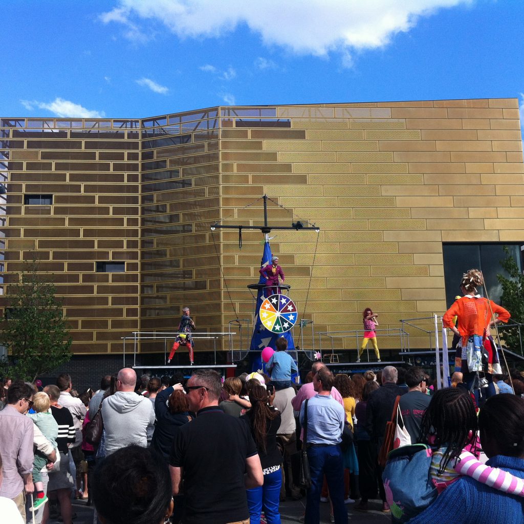 A large crowd of people on Giffin Square, outside a large gold building; Deptford Lounge.