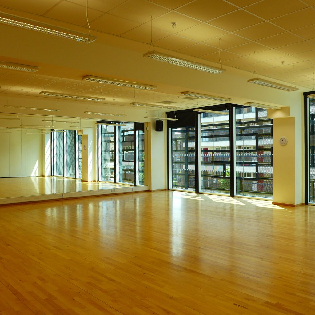 Large, mirrored, rehearsal room with wooden floor.
