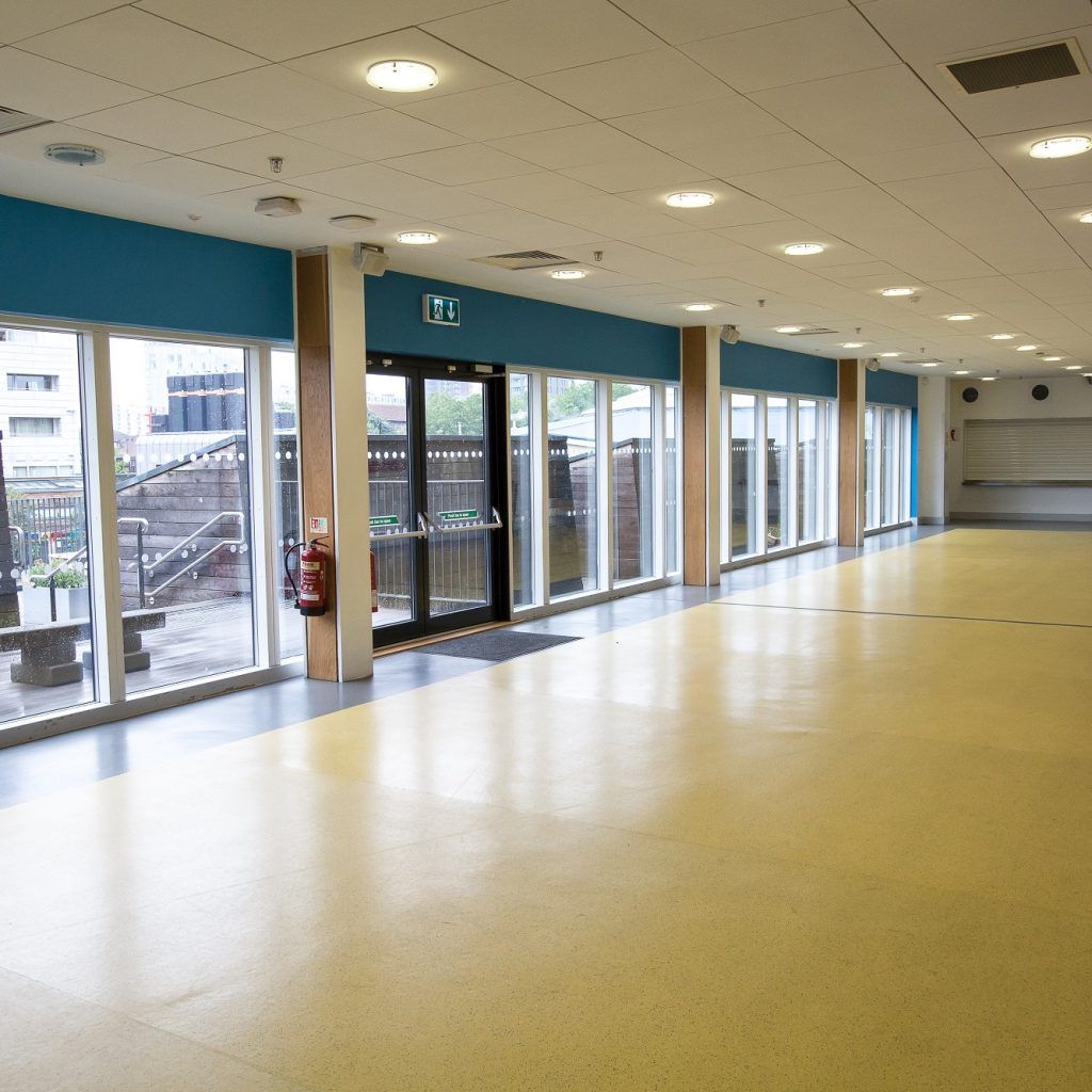 Long, thin room with yellow floor and large windows onto outdoor decked area.