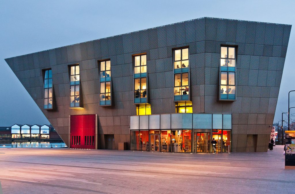 Large, modern, asymmetric building with steel cladding and warmly lit windows.