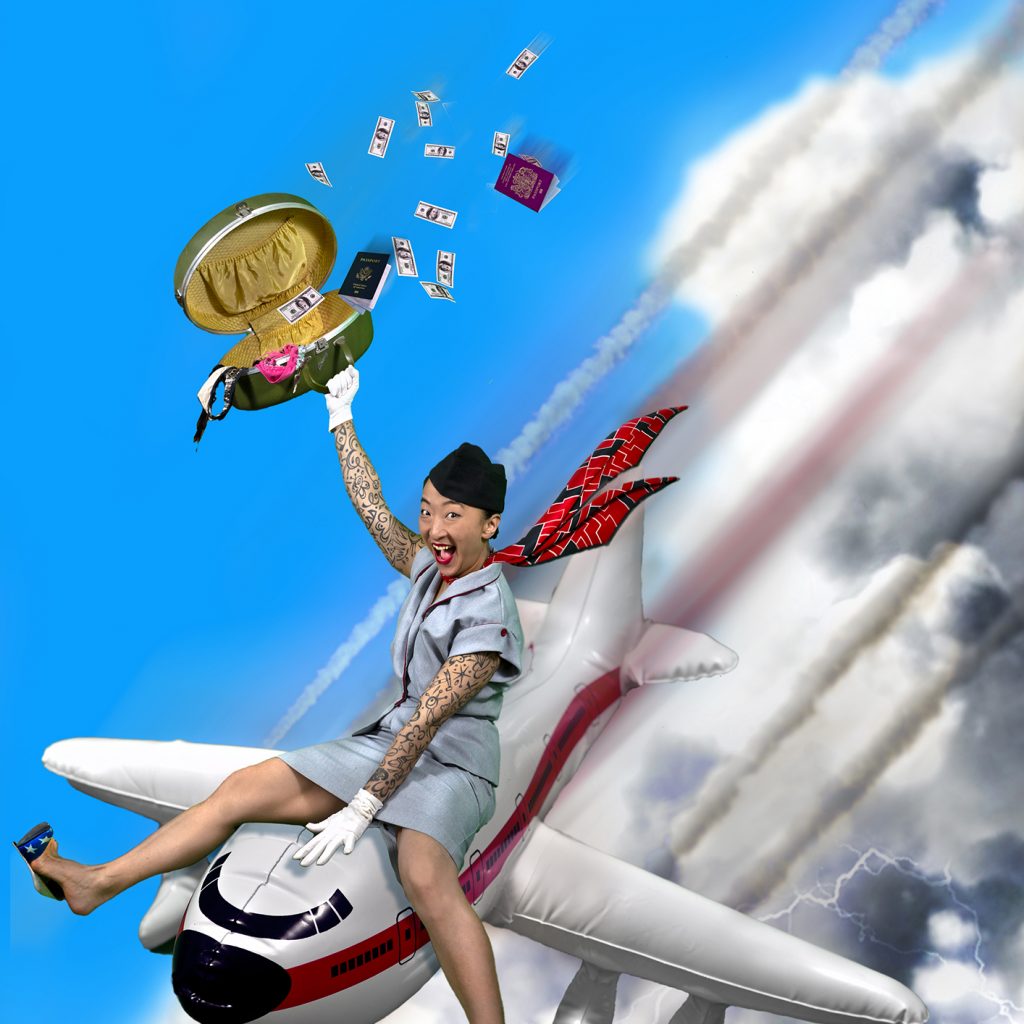 A man in stars and strips high heels and an air hostess uniform sits on top of an aeroplane as it flys through the sky.