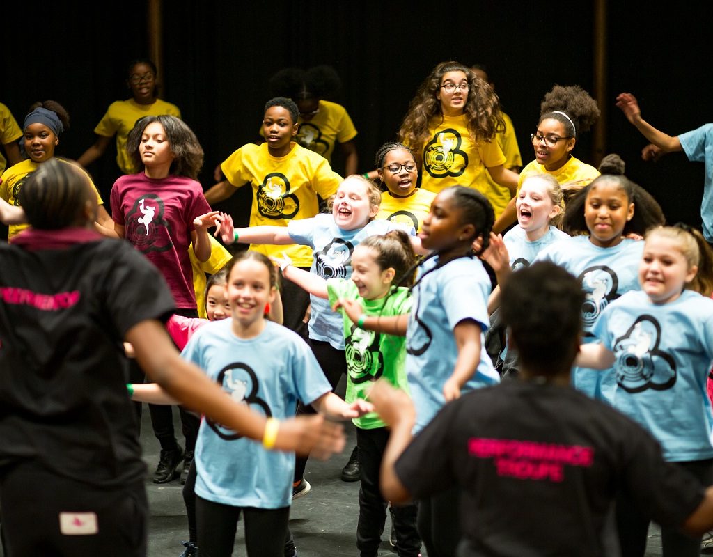 Image of a group of young people in different colour t-shirts are dancing and laughing.