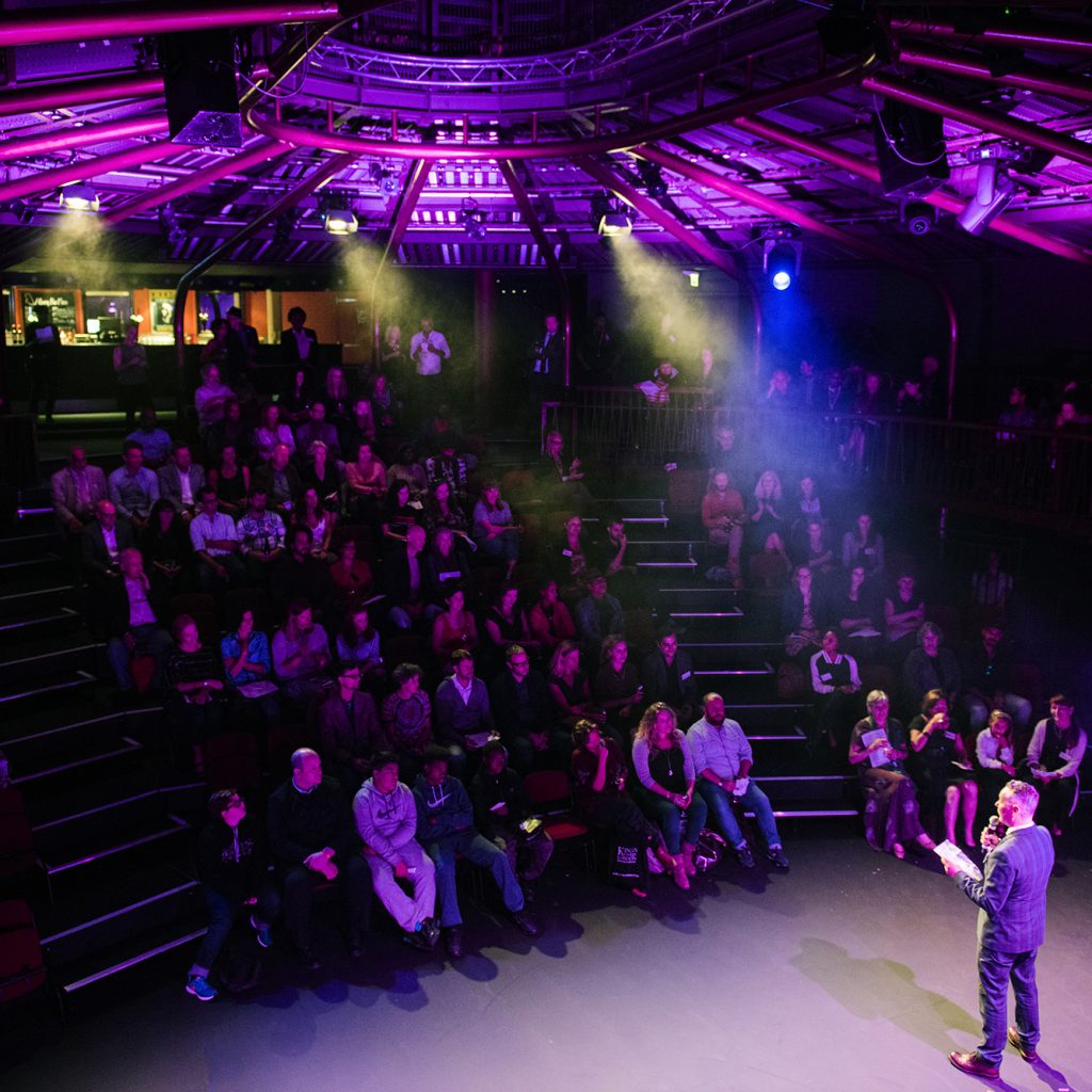 Man on stage at the Albany in front of large audience.