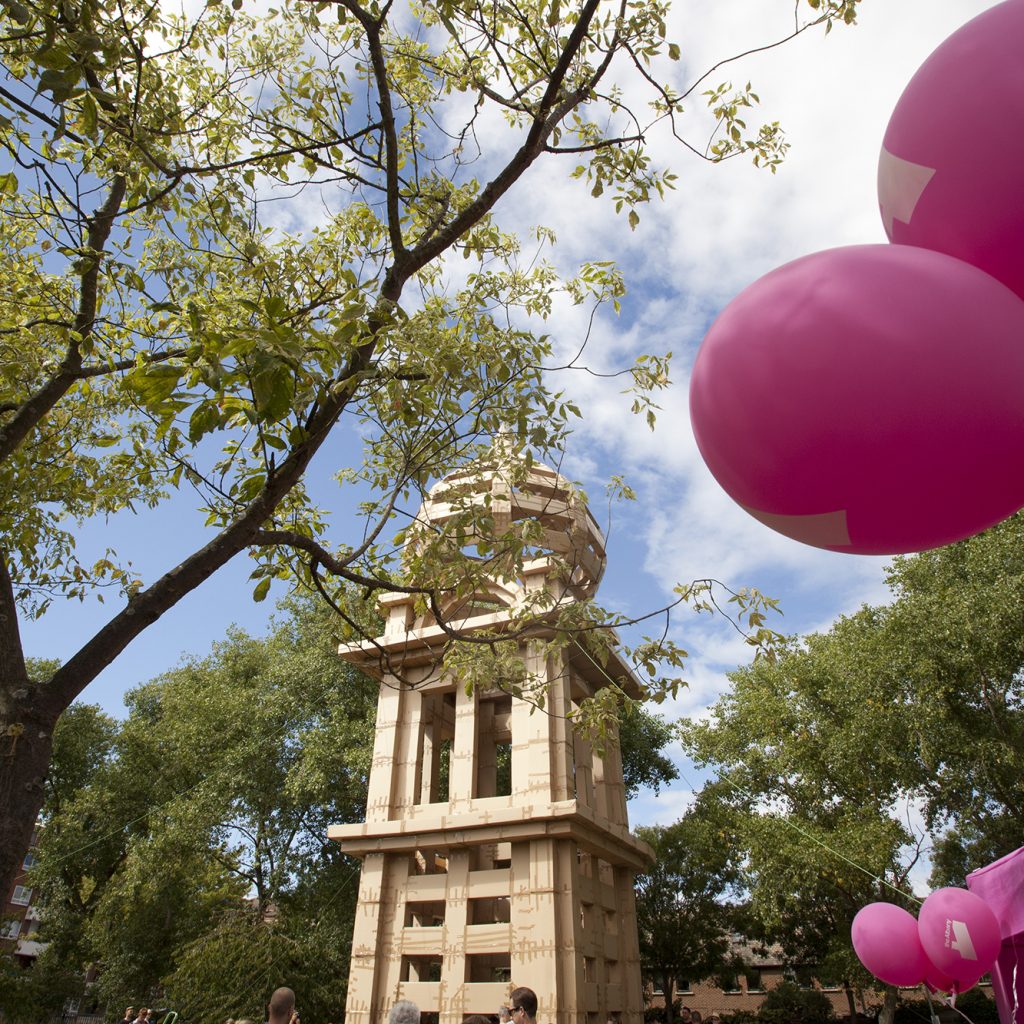 Blue sky, pink balloons and a huge cardboard tower built by members of the public in the Albany garden for a project called The People's Tower