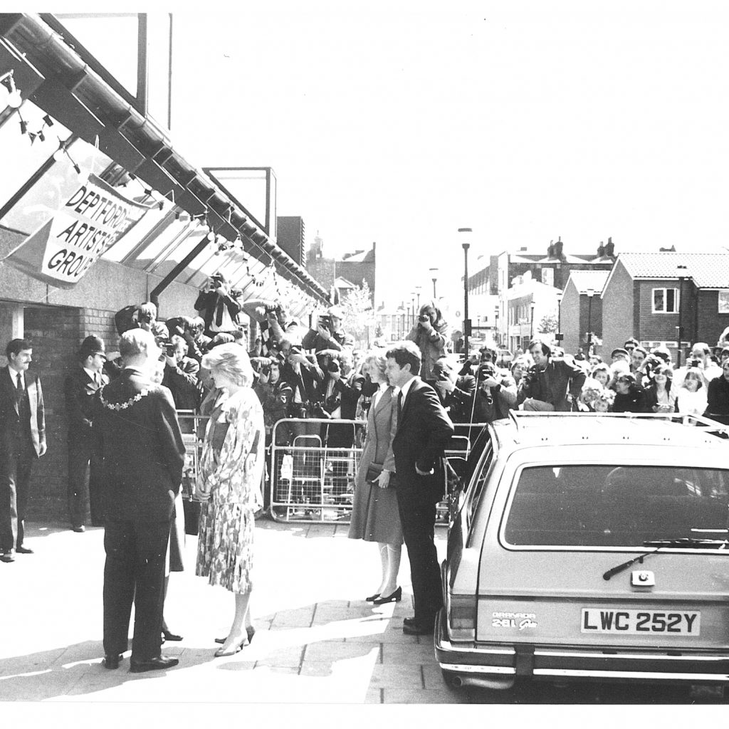 Black and white image: Princess Diana at the Albany entrance. Barriers and crowds in the background.