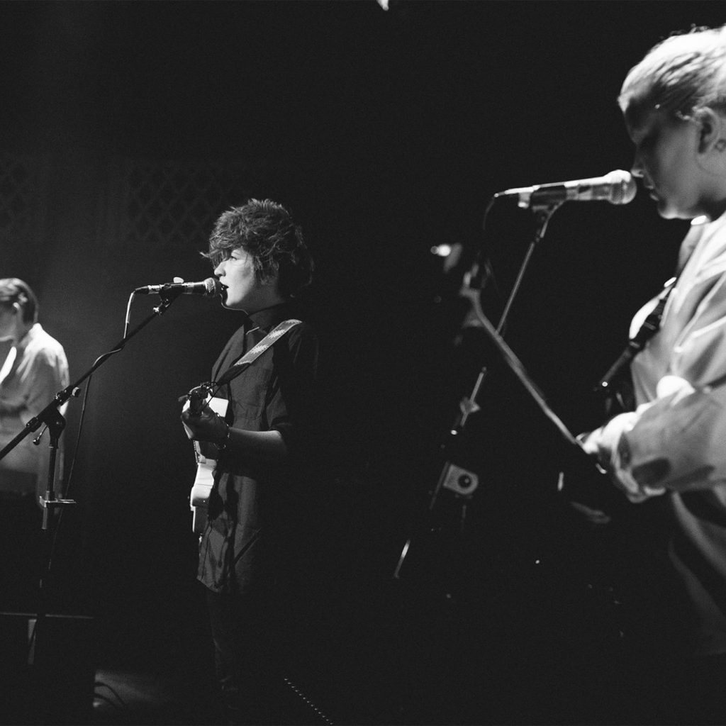 Black and white image showing three young, white, female musicians at microphones from the side on.