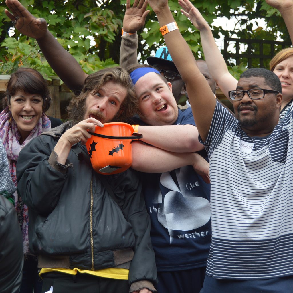 A group of Allsorts members smiling and waving their arms in the air. A man at the front is holding a halloween pumpkin style bucket.