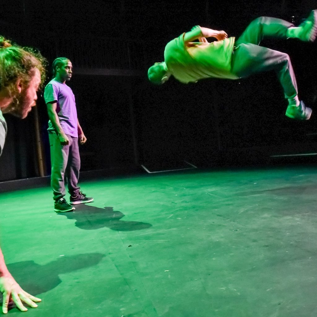 A performer flips through the air, two ,more look on.