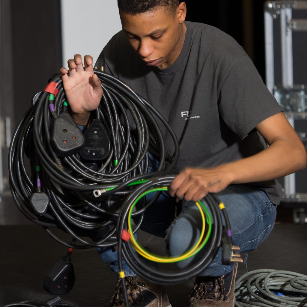A boy is crouched down holding cables