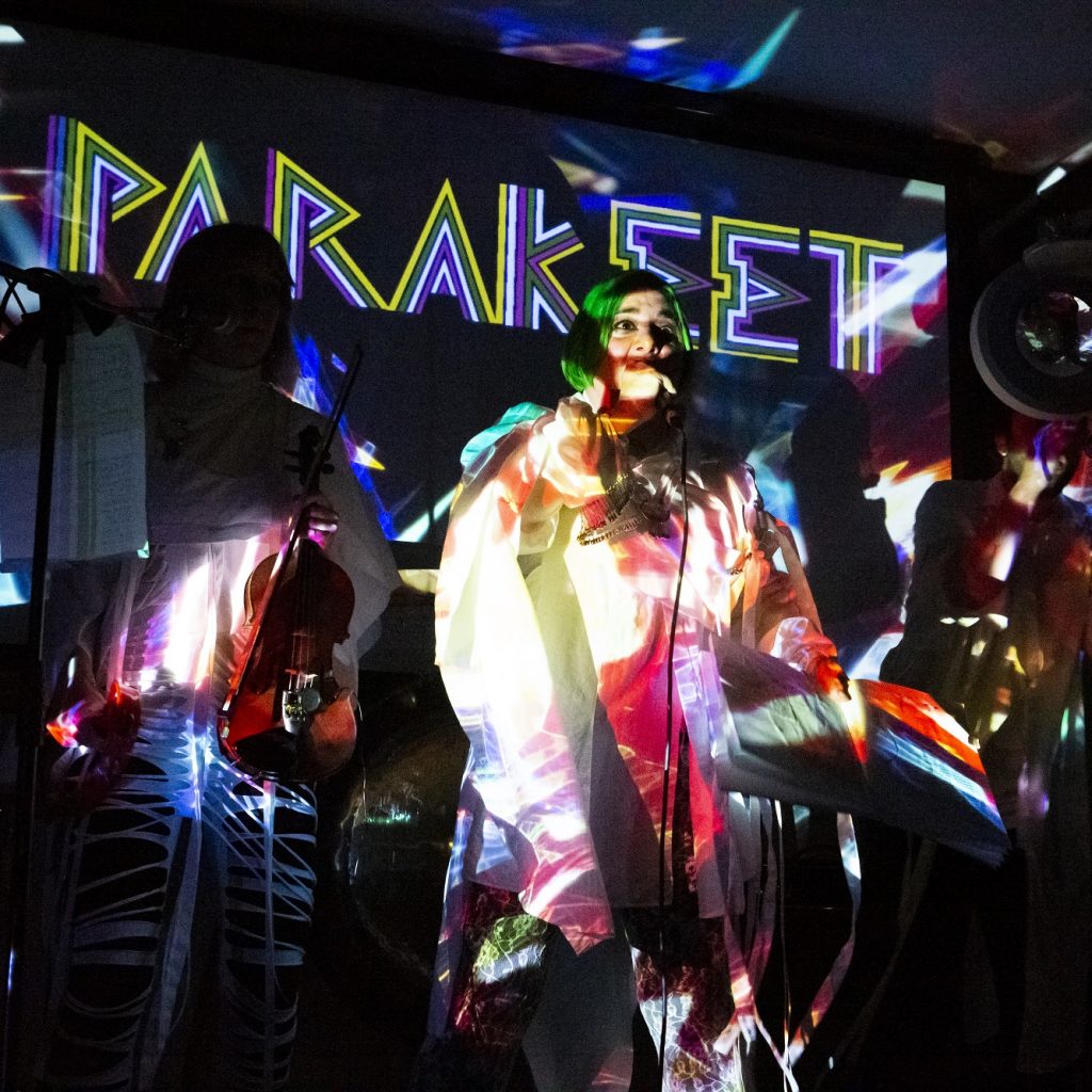 A woman with green hair, brightly lit on stage.