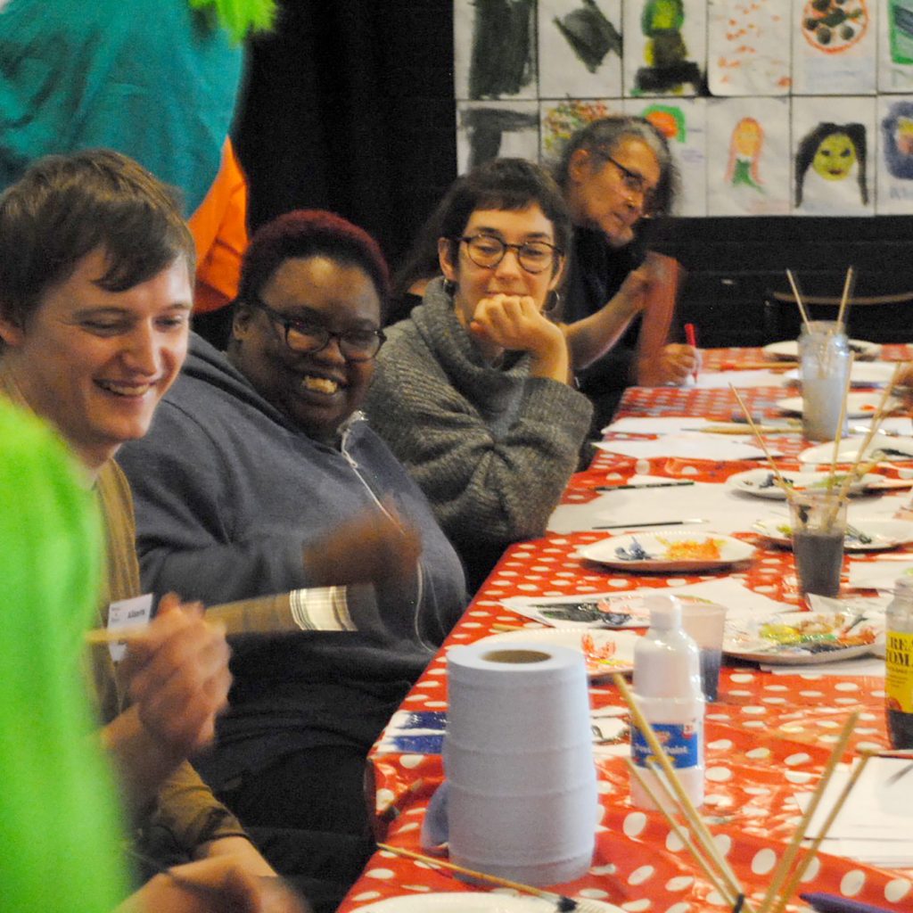 A group of people sit at a table engaging in craft activities.