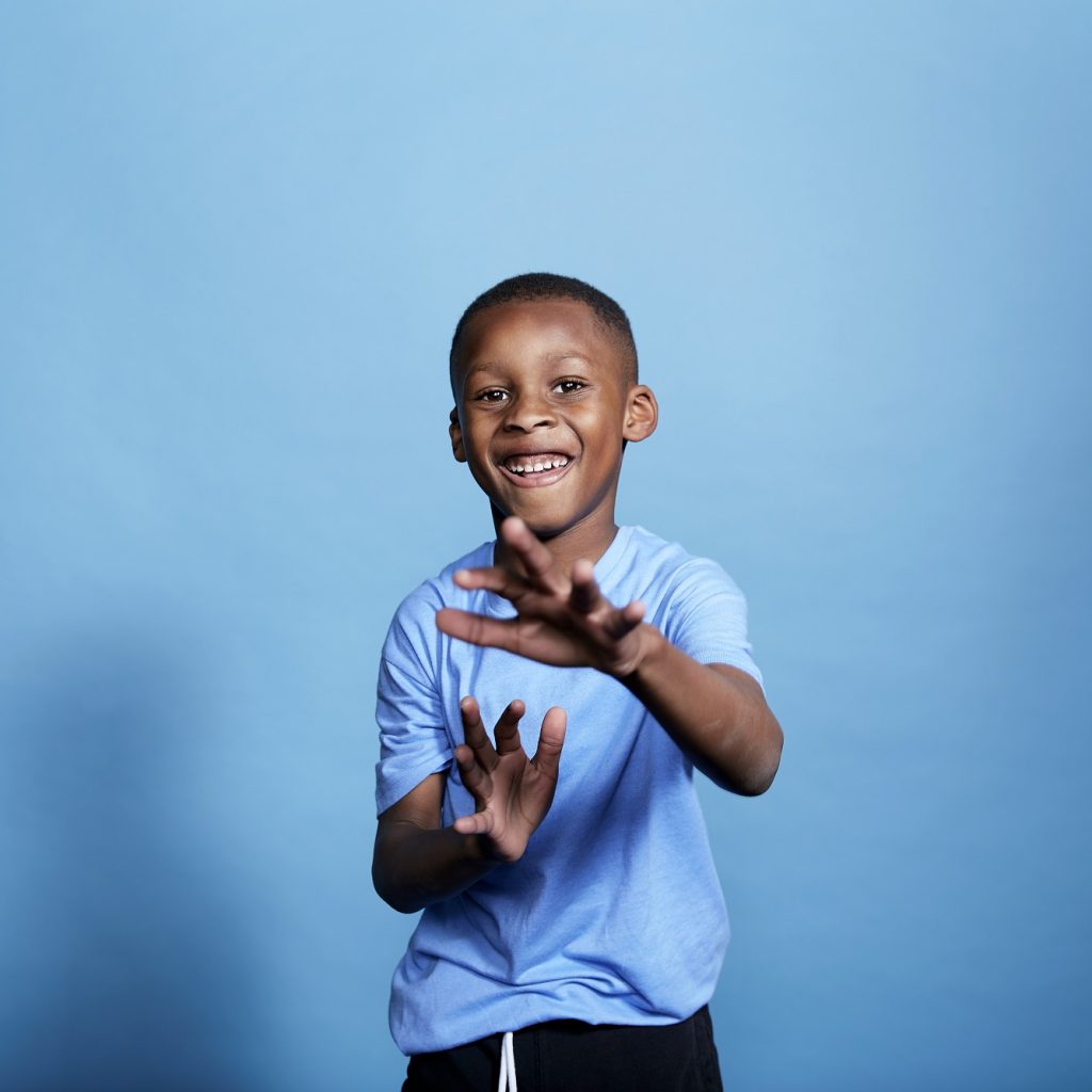 Image of a young boy standing in front of a blue backdrop, clapping.