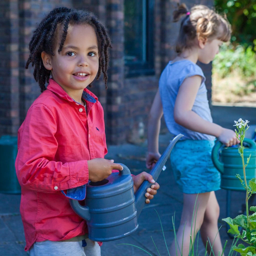 Image of a young child standing in a garden holding a watering can.