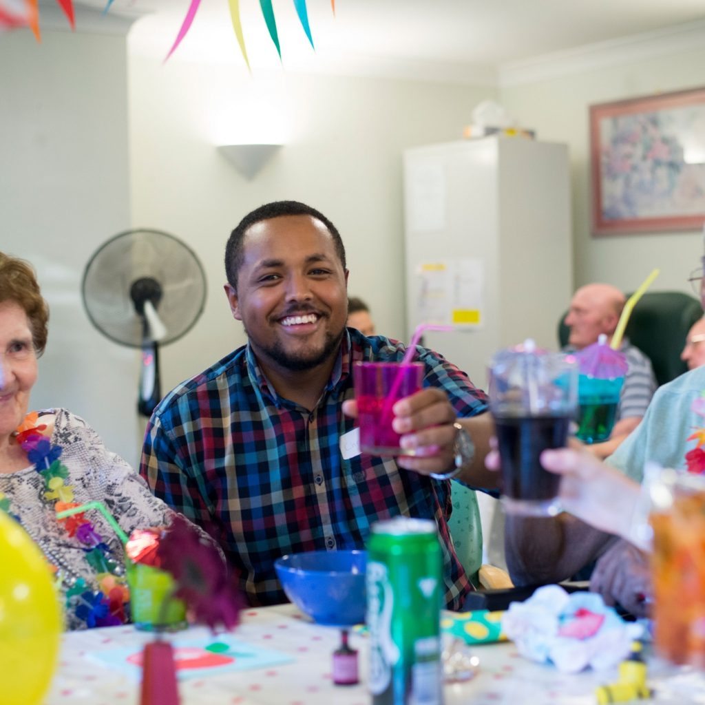 Image of 3 people sitting at a table at a party, holding drinks.