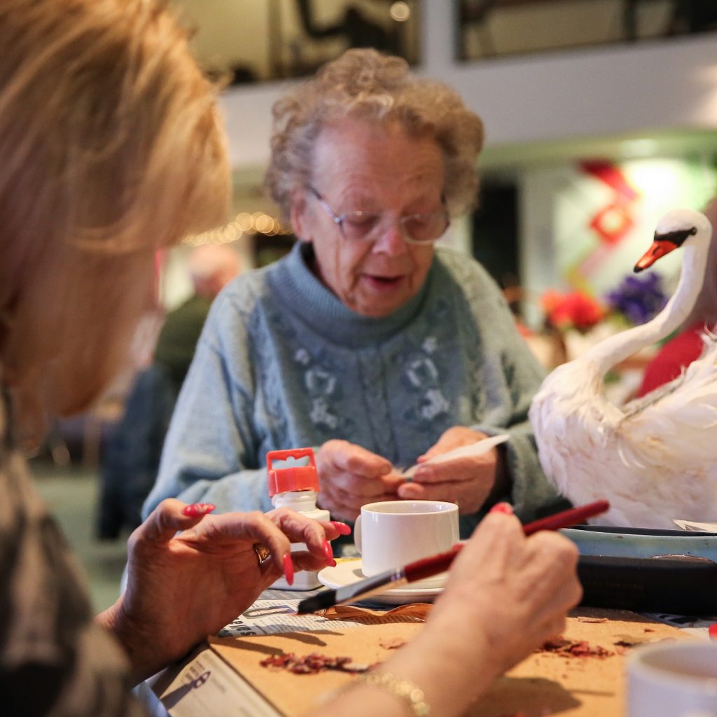 Image of two women, sitting at a table doing crafts.