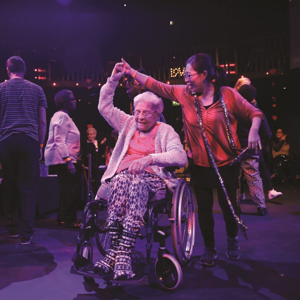 Image of 2 people dancing, one is an older woman in a wheelchair, the other holds her hand and is twirling her.