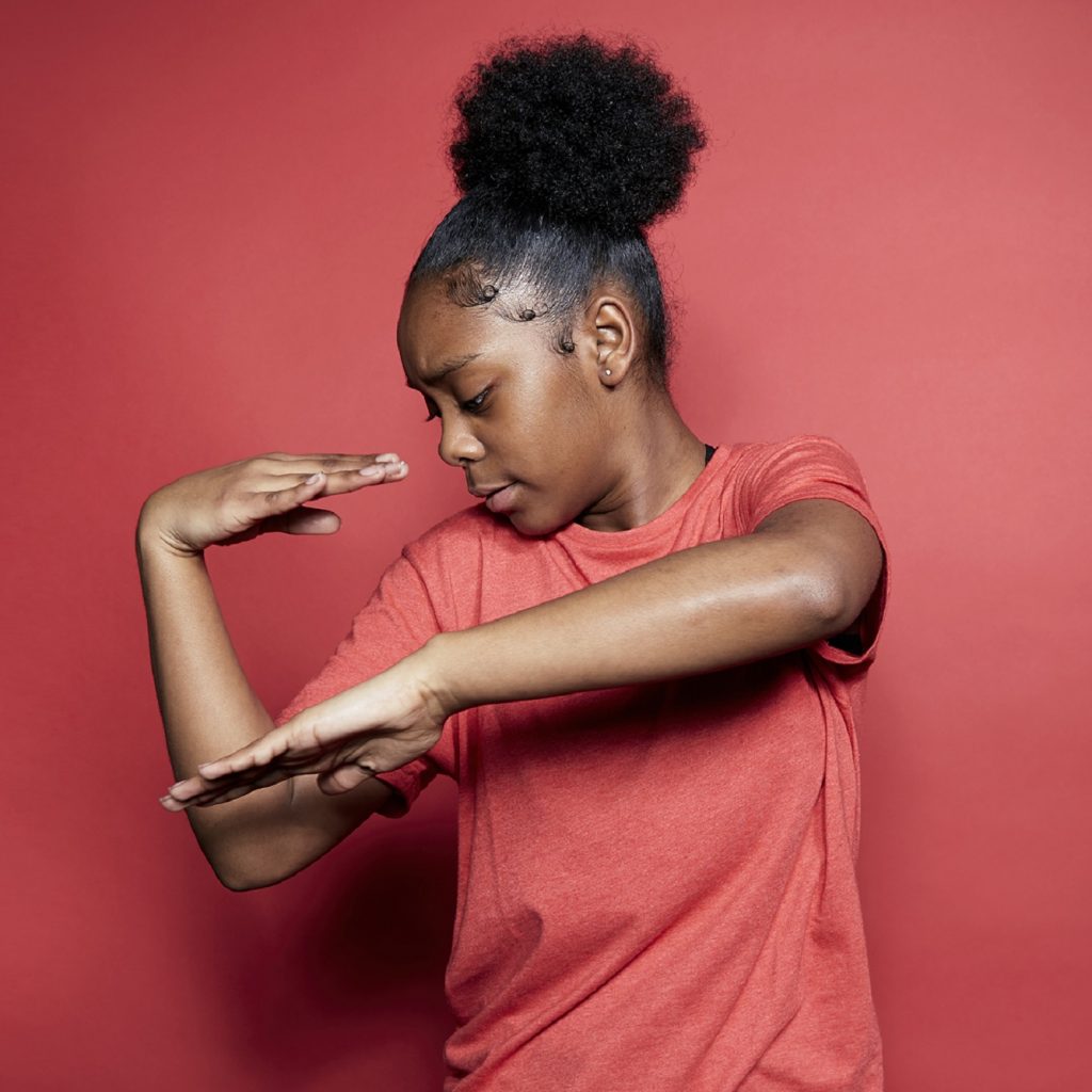 Image of a young girl doing a dance move against a red background.