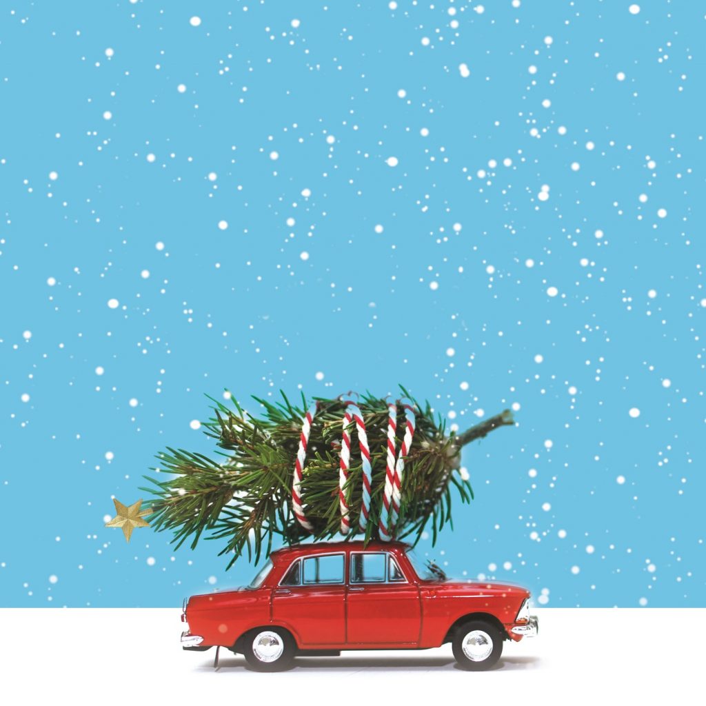An a image of a red car driving in snow with a Christmas tree wrapped on top of it. s