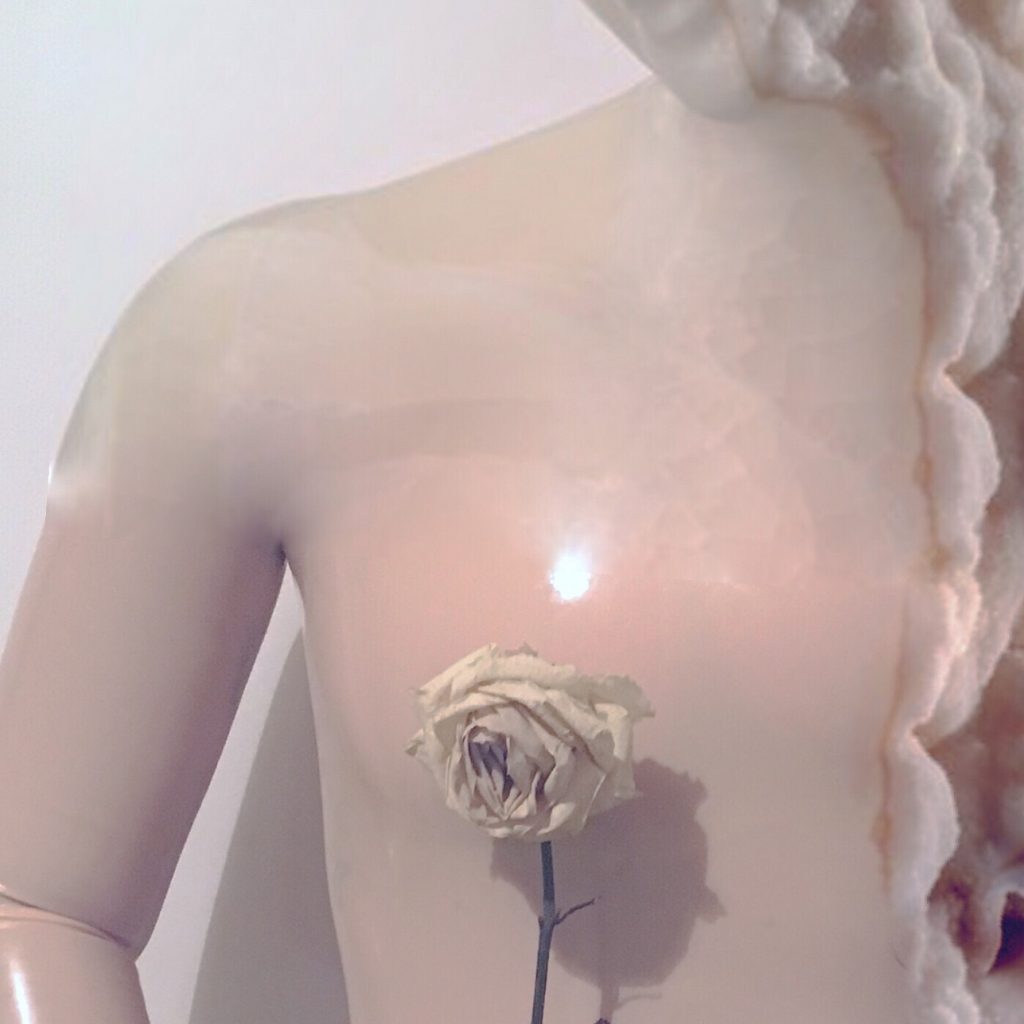 Image of a sculpture of a woman with a flower on it's chest and long blonde hair.
