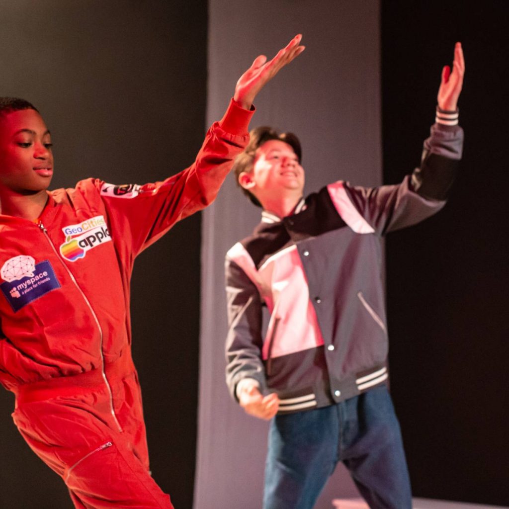 Image of two boys on stage dancing, both have their left arms in the air