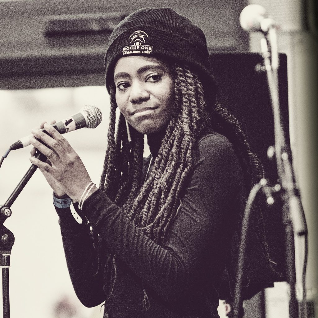 A young woman stands on stage with a microphone. Black and white photo