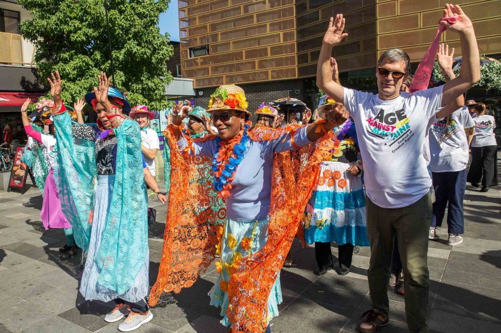 An group of older people in a carnival style parade, dressed to party in front of a blue sky.