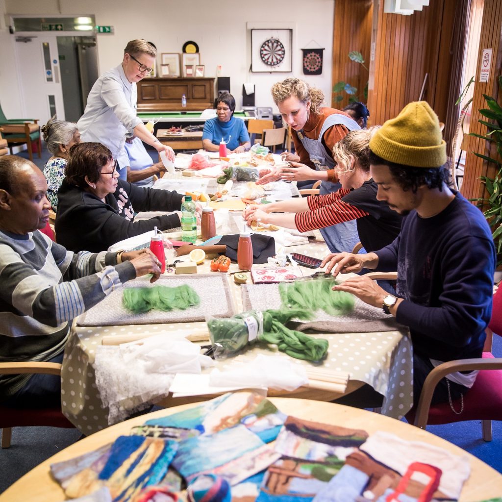 Adults of all ages sit working together on crafts at a long table.