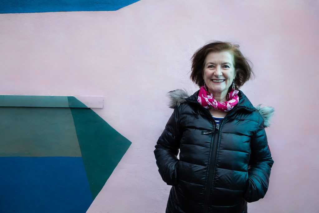 Angela Clerkin - a lady smiling with brown hair in a pink scarf and black puffer jacket