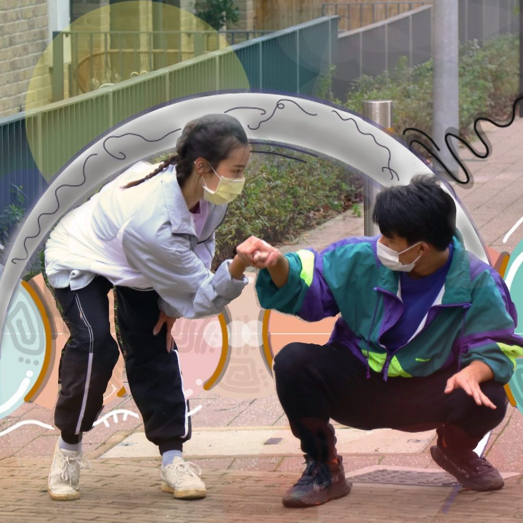 A girl with dark hair and pigtails wearing a face mask and tracksuit fist umps a man with short dark hair crouching down