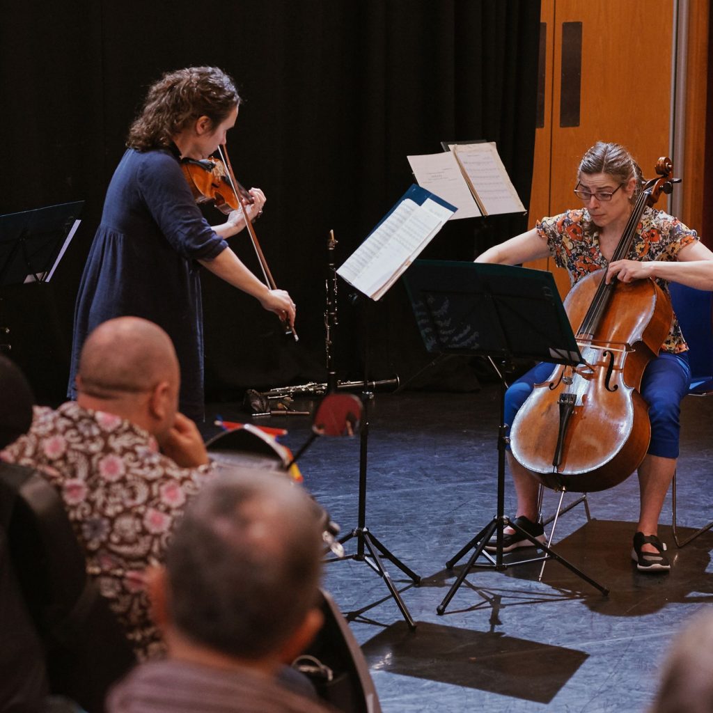 A woman plays a violin and another plays a cello in front of an audience