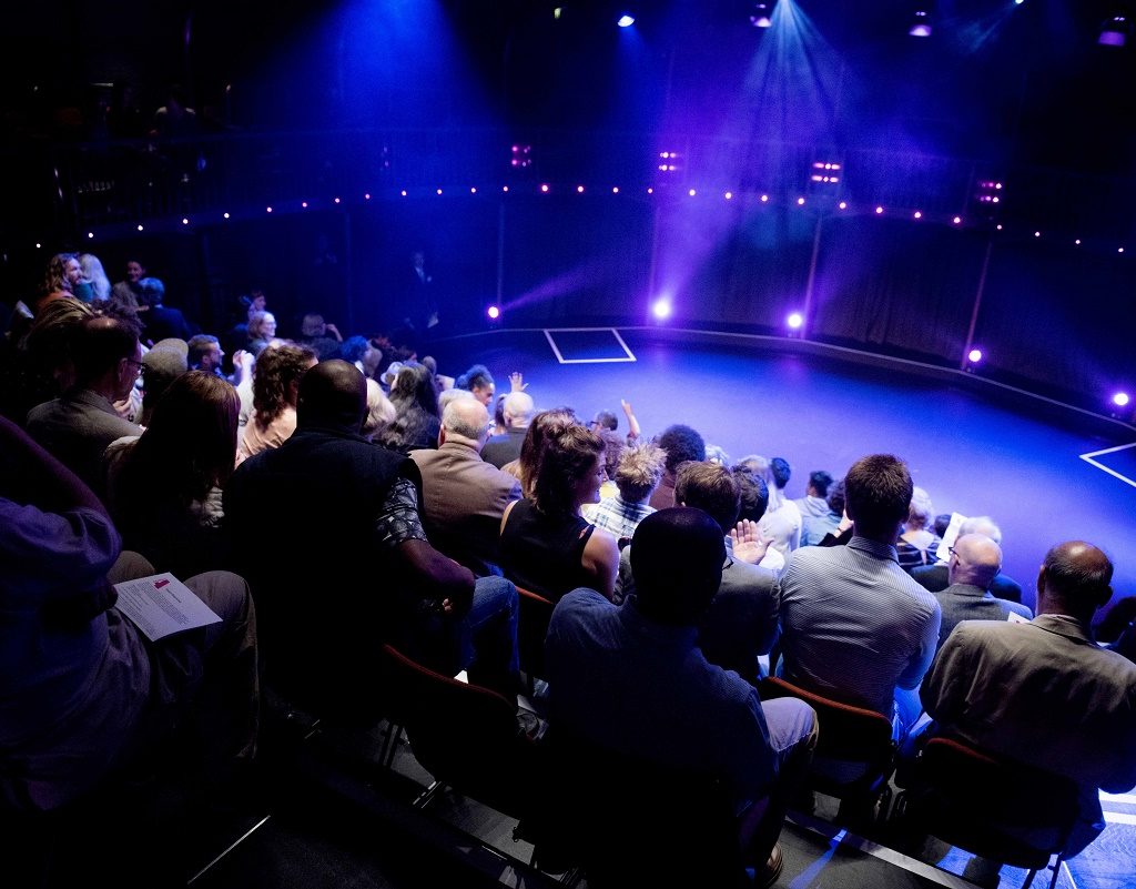 People sitting in our auditorium, facing the stage which is lit by purple light