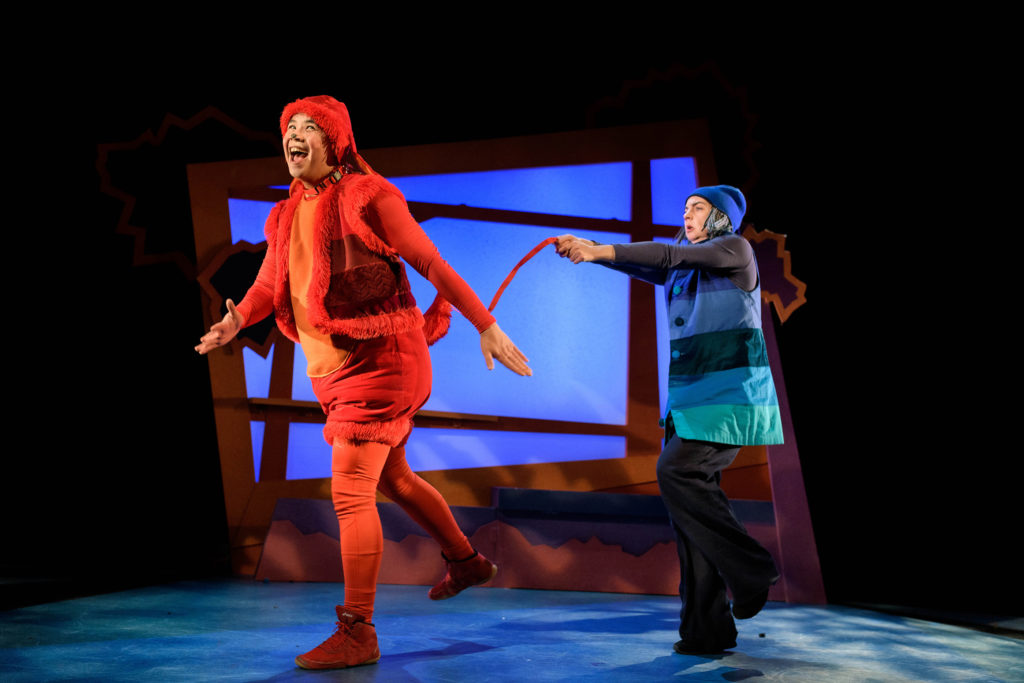 A photo from Can't Sit Still's production of Oh No, George! An actor dressed in blue holds the tail of another actor dressed as an orange dog.